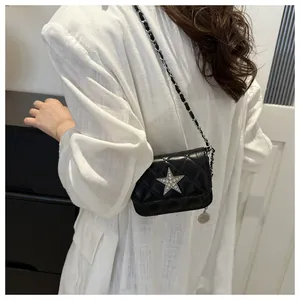 Detail of black quilted mini bag with rhinestone star and chain strap on white shirt