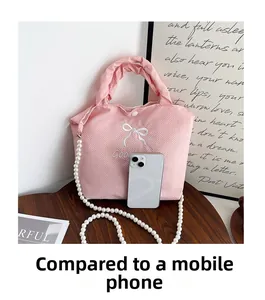 Detail of pink waffle texture handbag with pearl chain and bow compared with a phone