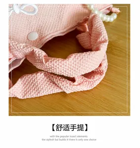 Detail of pink waffle texture handbag featuring white bow embroidery and pearl handle strap