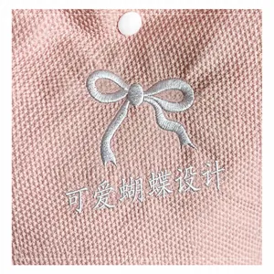 Macro detail of pink woven fabric with GoodLuck embroidery and a white button
