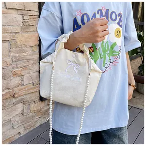 Detail of light beige waffle fabric bag featuring bow embroidery and a pearl chain strap