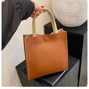 Close-up of brown leather tote bag with contrast stitching and beige handle on stand