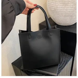 Close-up of minimalist black leather tote bag with dual handles and circular stitch detail