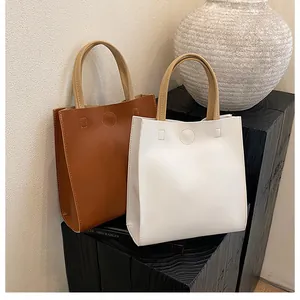 Detail of minimalist tote bags in brown and white with round buckles and fine stitching