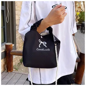Close-up of black waffle knit handbag featuring white bow embroidery and pearl chain strap