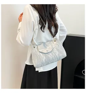 Detail der silbernen Schultertasche mit Faltenoptik und Goldkette am Model