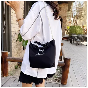 Detail of black canvas handbag with white bow embroidery and elegant pearl chain strap