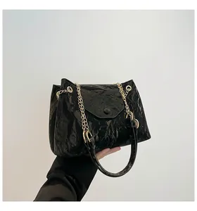 Detailaufnahme einer schwarzen Schultertasche in Knitteroptik mit zwei goldenen Ketten