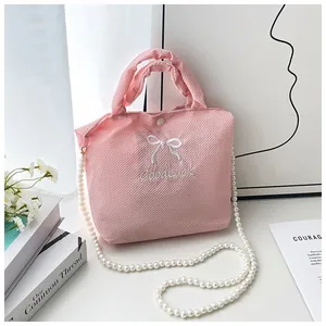 Macro detail of pink textured fabric bag with bow embroidery and pearl chain strap