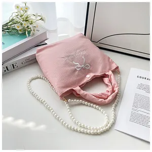 Detail of pink fabric handbag with white bow embroidery and elegant faux pearl strap