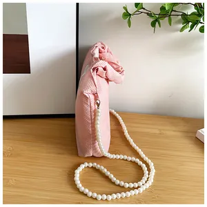 Detail of light pink textured fabric bag with elegant pearl chain and woven surface