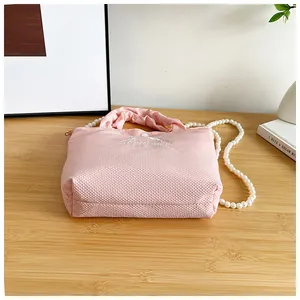 Detailed close-up of pink waffle fabric handbag with bow embroidery and pearl chain