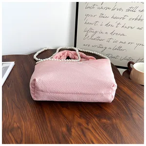 Pink quilted bow handbag with elegant pearl strap on wooden table, lifestyle view