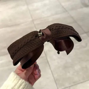 Détail d'une pince à cheveux double nœud en tricot marron et ruban de satin avec charme