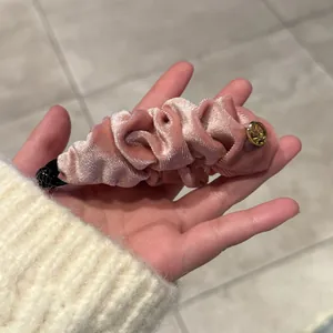 Gros plan sur une pince à cheveux banane en velours plissé rose avec logo doré et grip noir