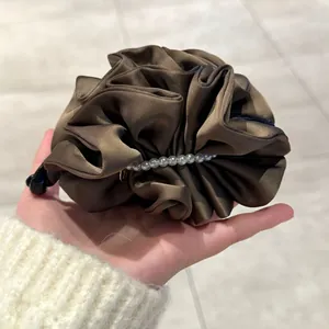 Détail d'une pince banane en satin plissé marron avec perles élégantes pour cheveux