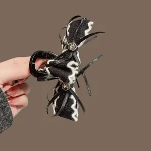 Pinza per capelli con fiocco di velluto, strass e trama ondulata tenuta in mano