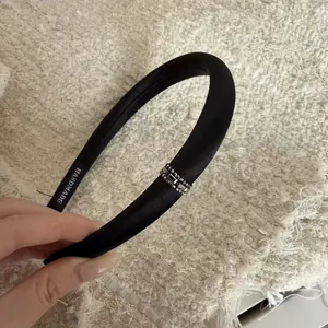 Detail showing the handmade label and silver rhinestone decor on a black satin headband