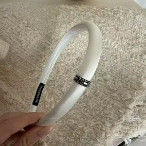 Elegant white satin padded headband featuring a sparkling dark rhinestone buckle detail