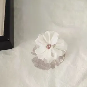 Close-up of white fabric flower hair claw with pink crystal center on textured fabric