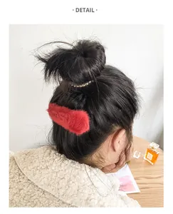Detail of red faux rabbit fur hair clip worn on straight black hair in a home setting