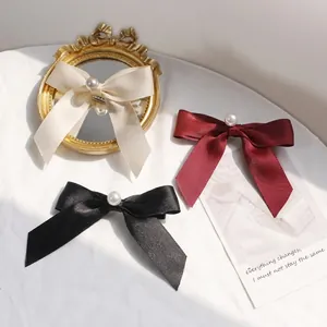 Close-up of satin bow hair clips in cream, red, and black with central pearl accents