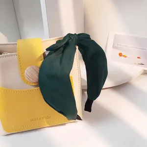 Detail eines dunkelgrünen Satin-Haarreifs mit Knoten neben einer modernen Handtasche