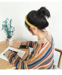Detail eines gelben Plüsch-Stirnbands kombiniert mit einem bunten Streifenpullover