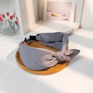 Eleganter grauer Stoff-Haarreif mit Knotendesign auf einem minimalistischen Holztablett
