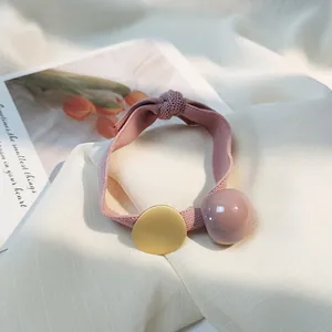 Détail de l'élastique à cheveux rose avec disque doré mat et perle sur tissu blanc