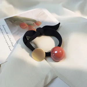 Détail de l'élastique à cheveux noir avec disque en métal doré et perle orange