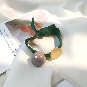Détail d'un élastique vert forêt avec disque en métal doré et perle acrylique brillante