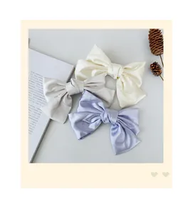 Detailed shot of three pastel satin bow hair clips in cream, grey, and lavender colors