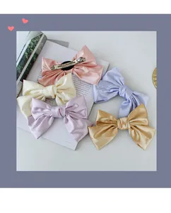 Detail of five satin bow hair clips in pastel pink, cream, lilac, blue and gold colors