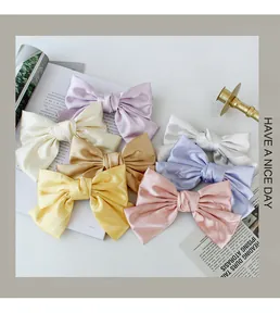 Detailed view of large satin bow hair clips in multiple pastel colors with silk texture