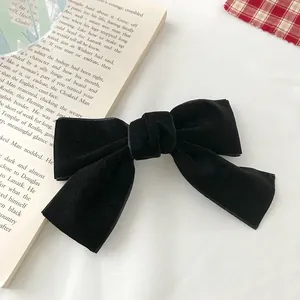 Detailed view of a black velvet bow hair clip on a white desk next to a vintage book