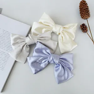 Three elegant satin bow hair clips in cream, grey, and lilac on a minimalist background