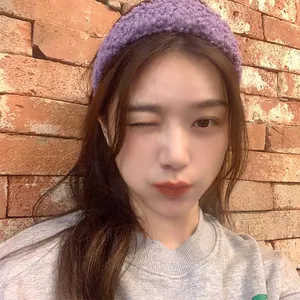 Close-up of a wide purple lamb wool headband shown on a model against a brick wall
