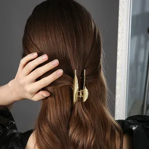 Dettaglio di una grande molletta per capelli dorata a forma di piuma su capelli castani