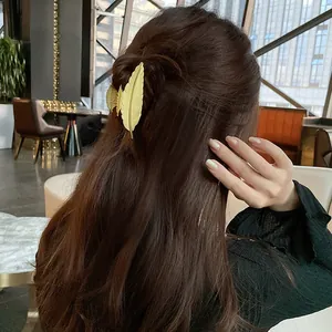 Elegante pinza per capelli a piuma dorata con trama metallica spazzolata su capelli castani