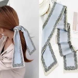 Detail view of light blue silk scarf featuring vintage patterns used as a hair tie and headband