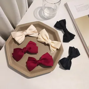 Three-layer bow hair clips in cream, wine red, and black on a minimalist tray