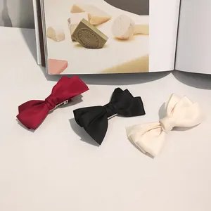 Three-layer bow hair clip set in red, black, and beige colors on a white minimalist surface