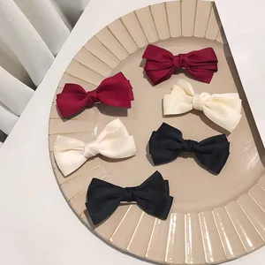 Detailed view of satin triple-layered bow hair clips in red, beige, and black on a tray
