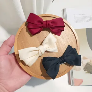 Detailed view of three-layered grosgrain bow hair clips in wine red, cream, and black