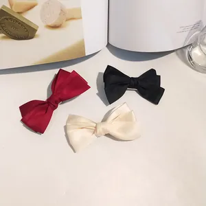 Detailed shot of triple-layer satin bow hair clips in burgundy, black and creamy white