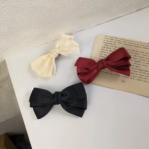 Detailed view of triple-layered ribbon hair clips in cream, burgundy, and black fabric
