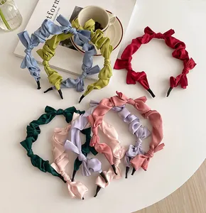 Detail of pleated satin bow headbands in various colors on a white minimalist desk