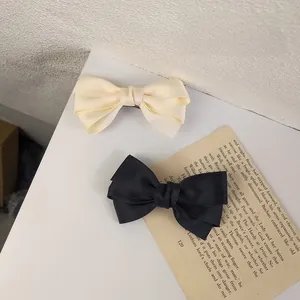 Detail of elegant triple-layered satin bow hair clips in beige and black colors