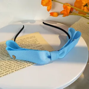 Détail du serre-tête à nœud bleu clair avec ruban gros-grain et pièce décorative en métal doré